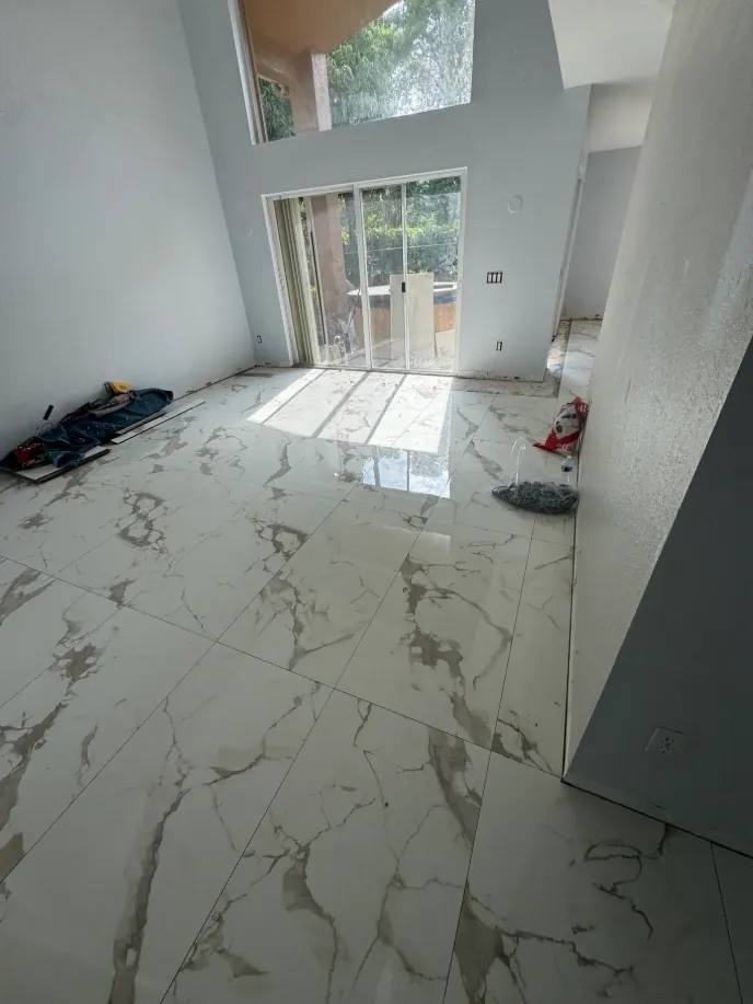 Bright room viewed from a doorway with white gray-veined flooring leading toward windows