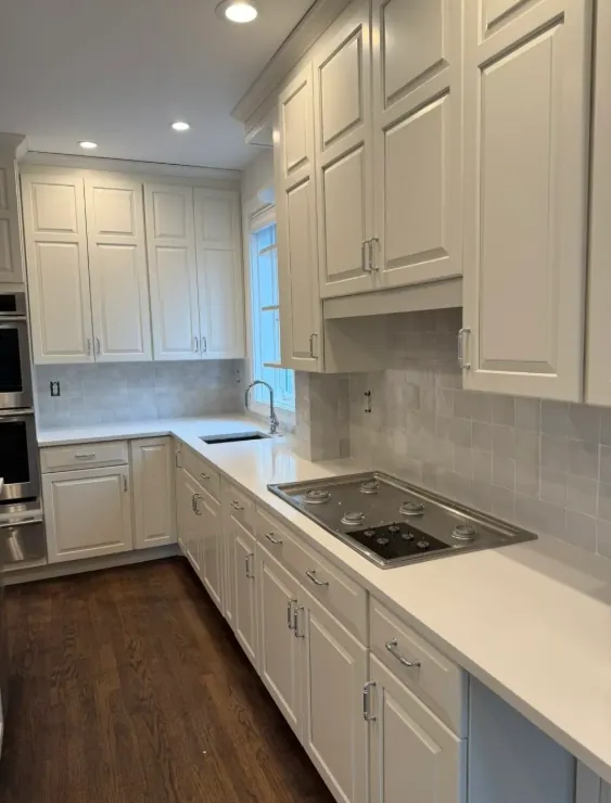 Second kitchen angle showing light cabinets, bright counters, and medium-brown linear flooring