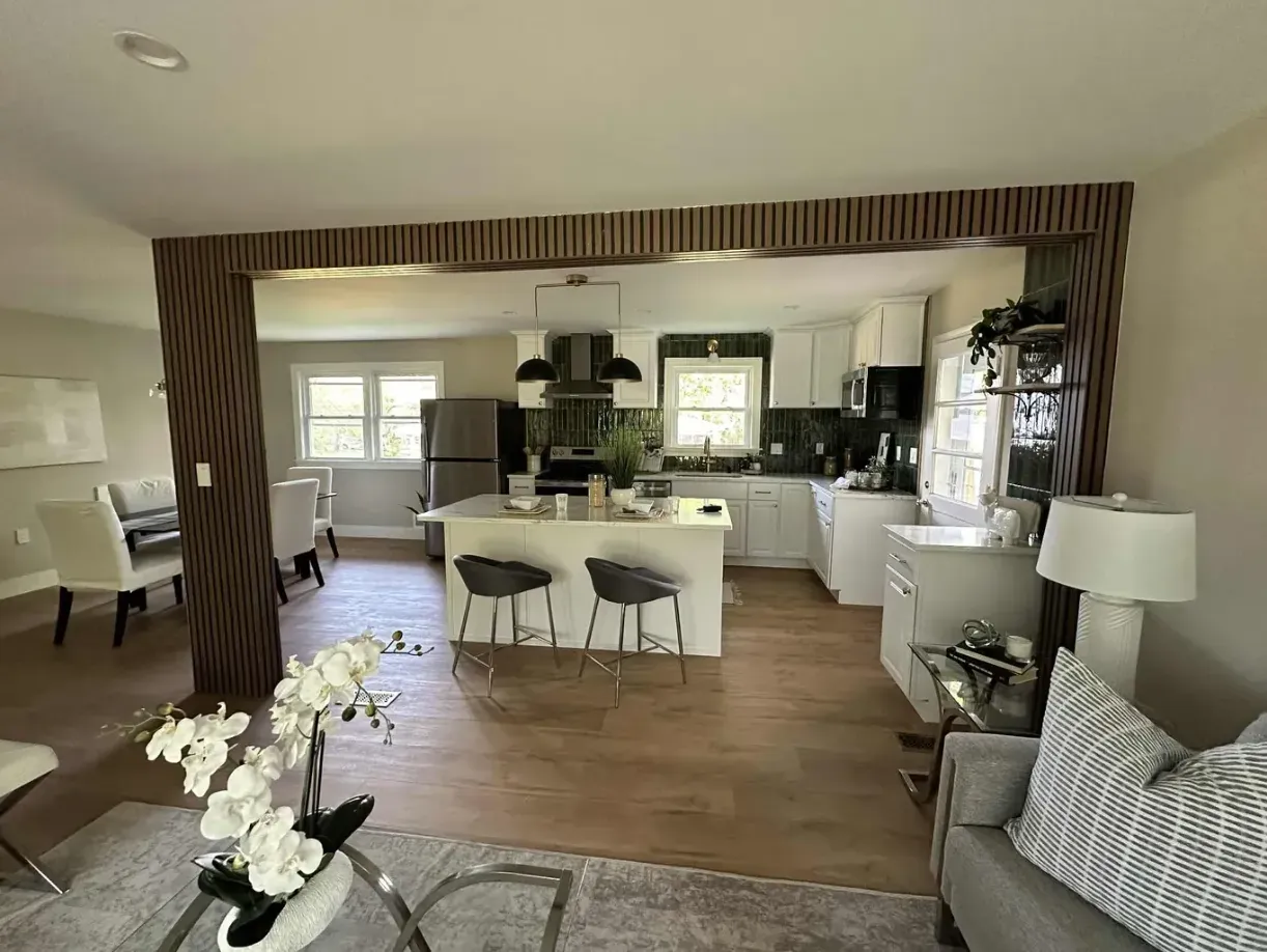 Open kitchen and dining area with medium-brown floor, light cabinetry, island seating, and a living area beyond