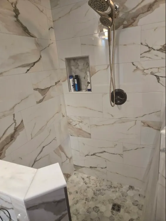 Glass shower with white gray-veined wall surfaces and black shower fixtures